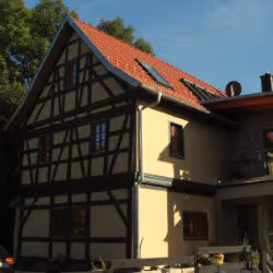 Traditional half-timbered house with beige walls and red-tiled roof under a blue sky.