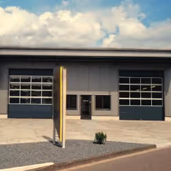 Building facade with two large garage doors, one with many window panels, under a cloudy sky.
