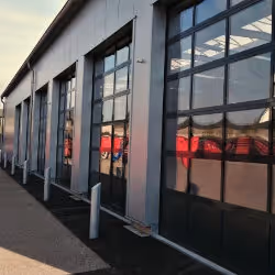 Exterior view of a modern industrial building with large glass-panel garage doors reflecting the sunset.