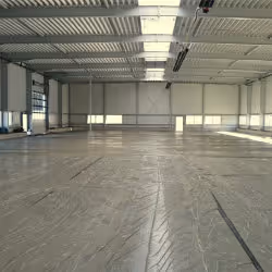 Spacious empty industrial warehouse with high ceiling and large windows.