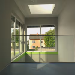 View from inside a room with large windows and a skylight looking out onto a house and green trees.