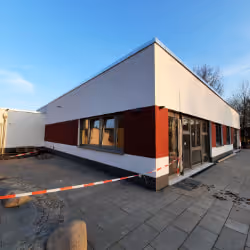 Modern single-story building with white and dark red exterior walls and large glass windows under a clear blue sky.