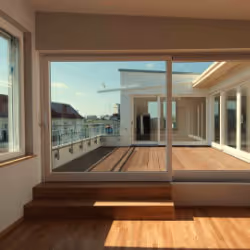 Modern balcony with wooden floor and glass sliding doors overlooking surrounding buildings and sky.