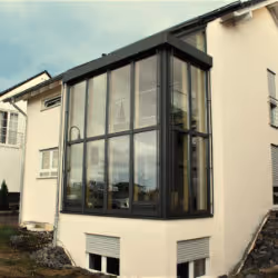 Glass-enclosed modern sunroom extension on the corner of a white two-story house.